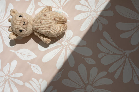 Matuu Warm Beige wallpaper shown flat with white daisy pattern and teddy bear – half in shadow for natural effect.