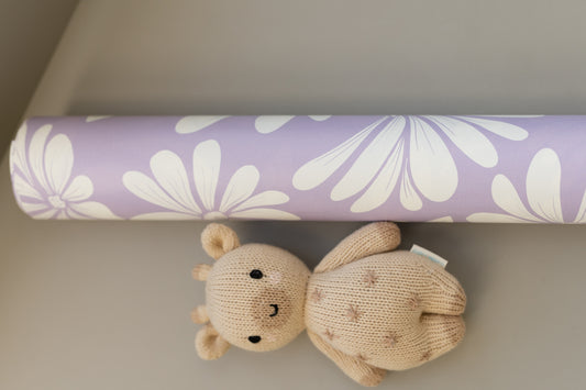 Close-up of Matuu’s Lilac Mist wallpaper with white daisies on a lilac base, partially shaded, with a small teddy bear.