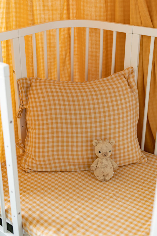 Crib with yellow checkered bedding and a teddy bear