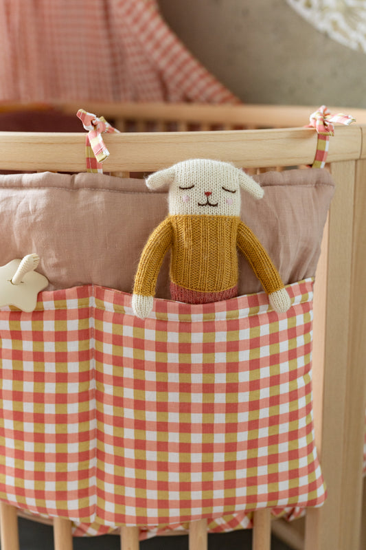 Close-up of Matuu crib organizer – rust gingham pockets with fabric ties and cuddly doll inside