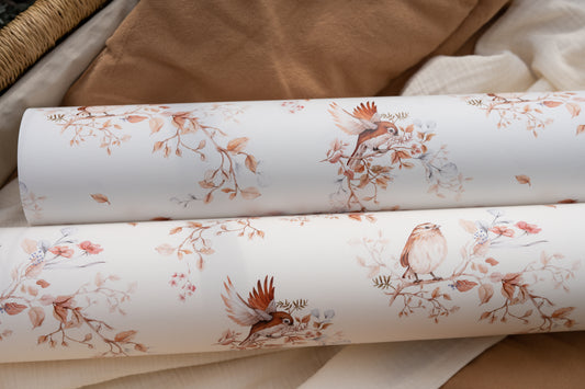 Close-up of several wallpaper rolls in a sand and beige bird-and-branch pattern.