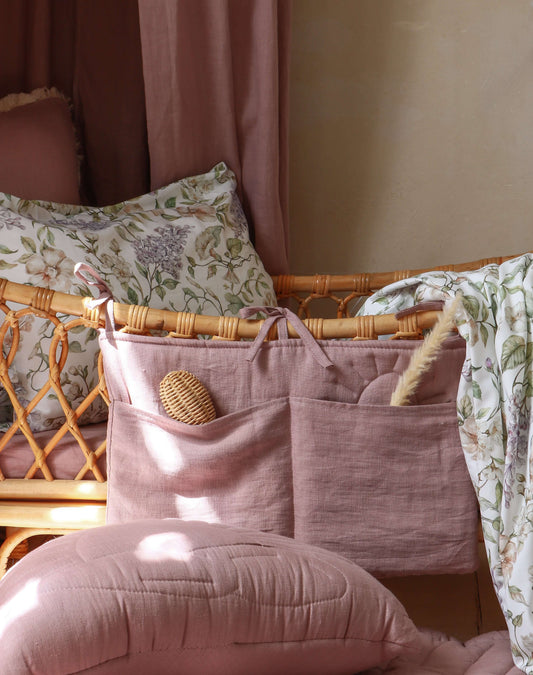 Lilac Sun crib organizer hanging on a rattan crib – linen bed pocket in muted lilac with two front pockets, styled in a cozy nursery with butterfly wall decor.