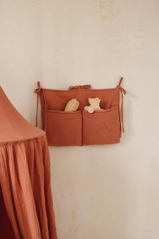 Matuu bed pocket in terracotta muslin – mounted on the wall with toys inside.