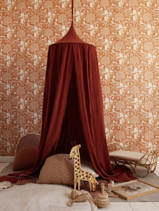 Matuu – Childhood Dreams wallpaper on terracotta wall with burgundy canopy and giraffe toy