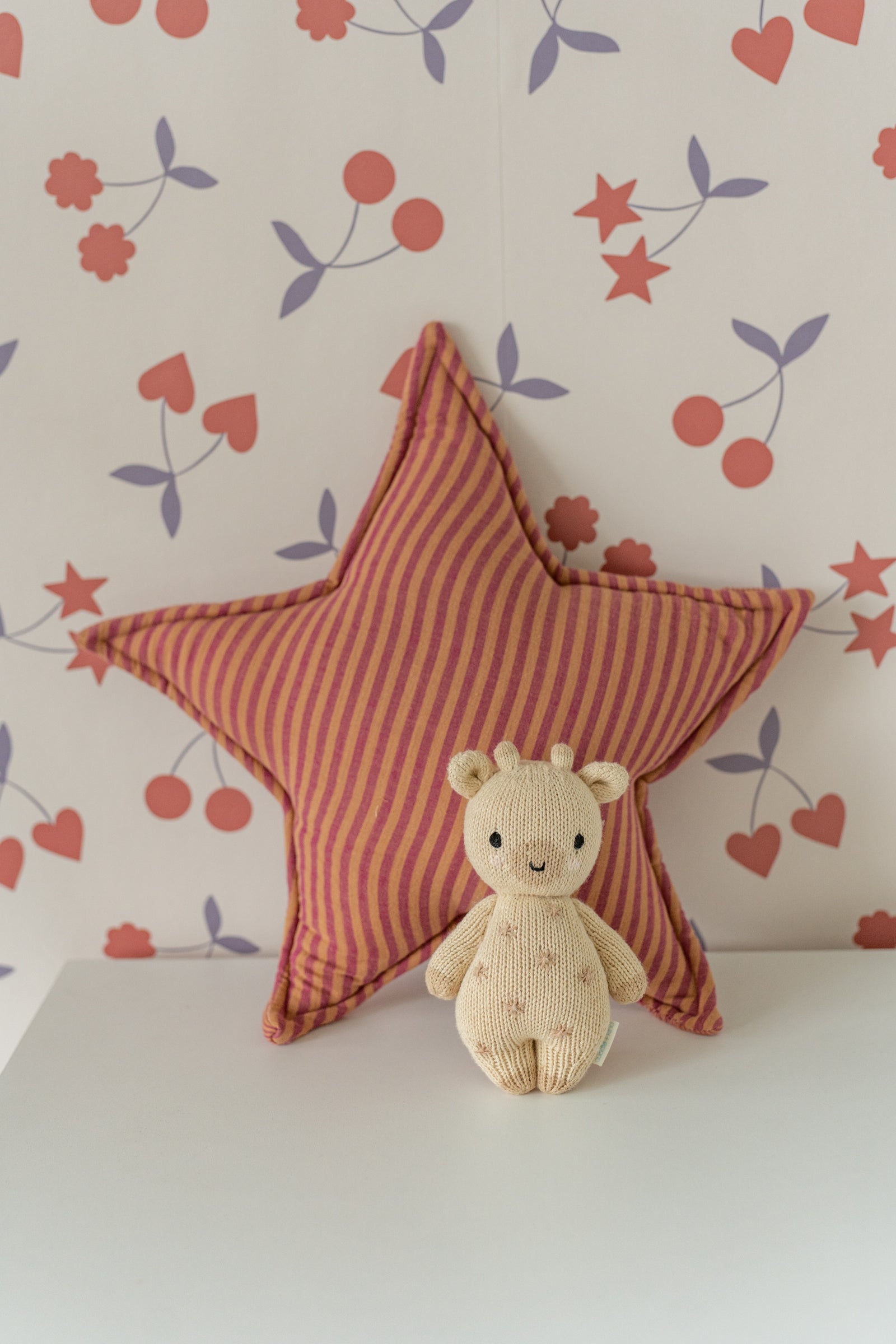 Decorative Matuu star pillow in rust on a dresser, with cream wallpaper featuring small hearts in the background