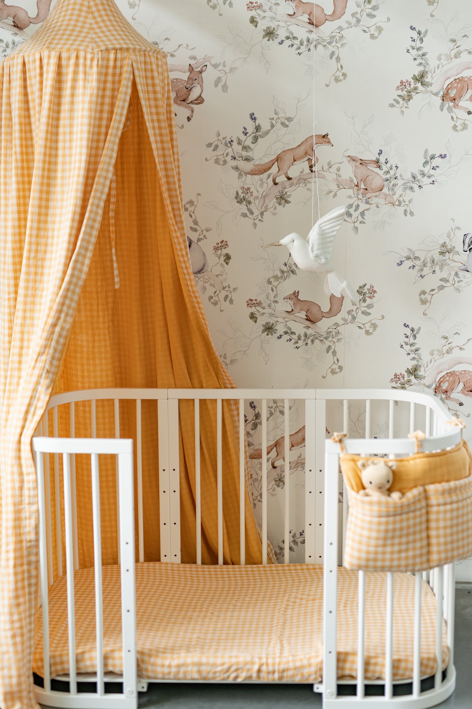 Nursery with a white crib, yellow checkered canopy, and floral wallpaper.